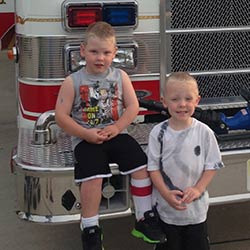 Two boys pose with a fire engine