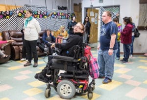 Woman in a motorized wheelchair at a 1950's sock hop themed party, several other guests are with her on the dance floor.